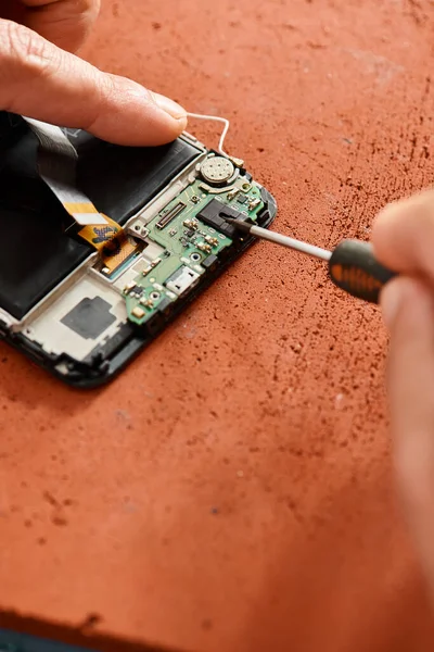 Обрезанный вид профессионального ремонтника, открывающего сломанный сотовый телефон с отверткой в мастерской — стоковое фото