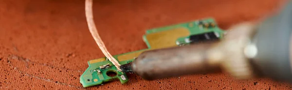 Soldering iron near microscheme of electronic device on table in repair workshop, horizontal banner — Stock Photo