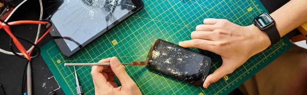 Vue partielle du technicien débranchant l'écran tactile cassé du smartphone dans l'atelier de réparation, bannière — Photo de stock