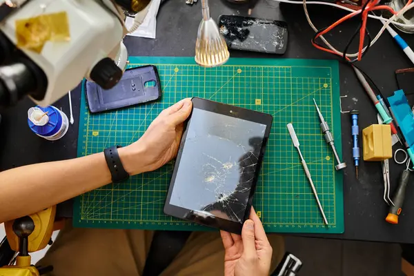 Cropped view of skilled technician holding digital tablet with broken touchscreen in repair shop — Stock Photo