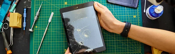 Partial view of experienced technician holding digital tablet with broken screen in workshop, banner — Stock Photo