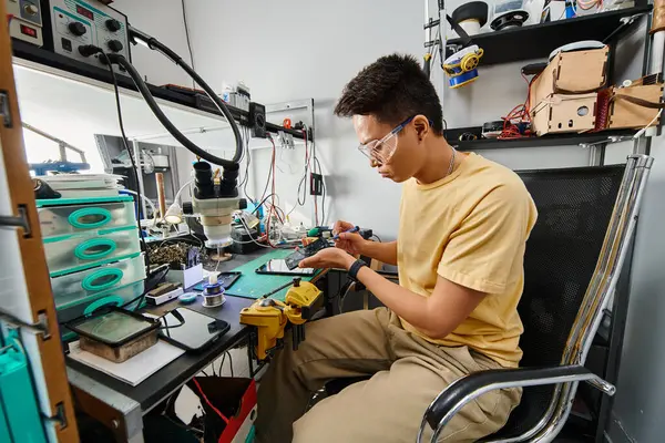 Professional asian technician in goggles maintaining electronic devices at workplace in repair shop — Stock Photo