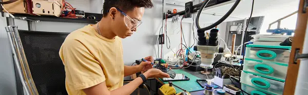 Skilled asian technician in goggles working with electronic devices in repair workshop, banner — Stock Photo