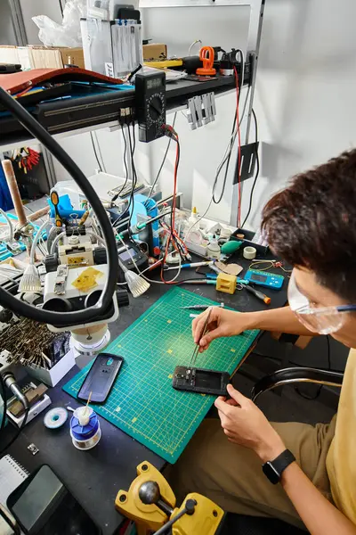 Experto asiático técnico en gafas de trabajo con roto smartphone y pinzas en su propio taller de reparación - foto de stock