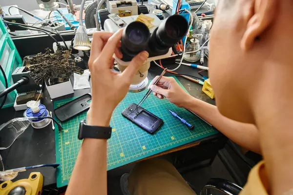 Vista posteriore di esperto tecnico con microscopio che fa la diagnostica di smartphone in officina di riparazione — Foto stock