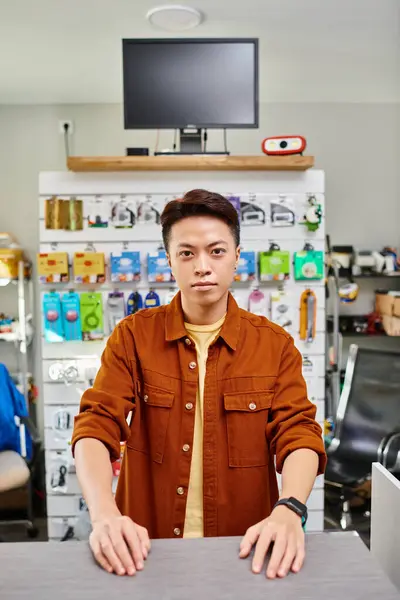 Confiado asiático hombre mirando cámara en privado electrónica tienda con surtido de electrónica - foto de stock