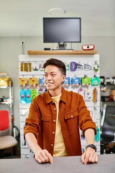 Joyeux asiatique entrepreneur regardant loin près du comptoir de magasin privé d'électronique et d'accessoires — Photo de stock