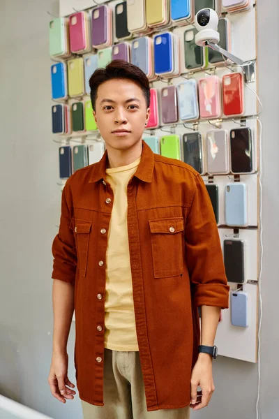 Успішний азіатський підприємець, дивлячись на камеру біля асортименту телефонів в приватному магазині — стокове фото