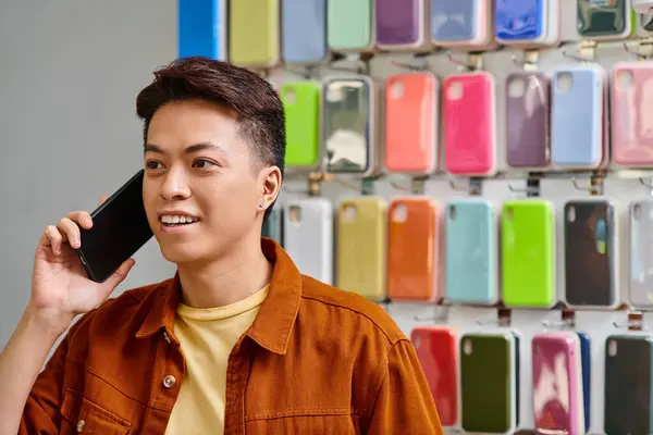 Позитивний азіатський бізнесмен розмовляє на смартфоні поблизу вітрини з телефонами в приватному магазині — стокове фото