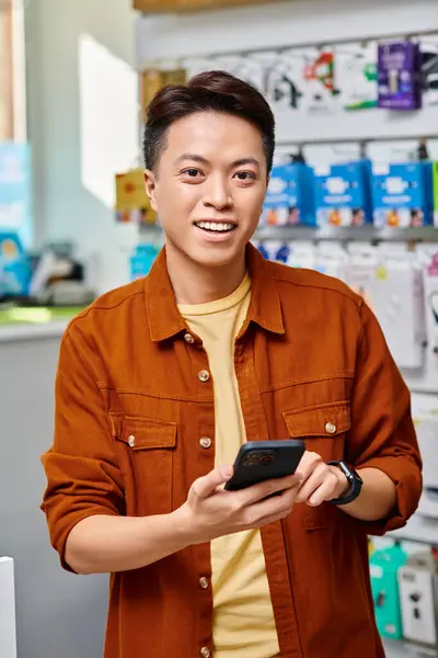 Alegre asiático hombre de negocios con móvil sonriendo a cámara en privado electrónica tienda - foto de stock