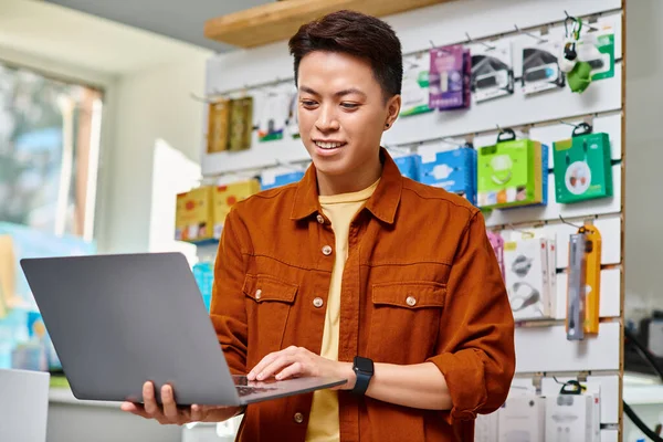 Heureux asiatique entrepreneur en utilisant ordinateur portable debout dans son propre magasin d'électronique, concept de petite entreprise — Photo de stock