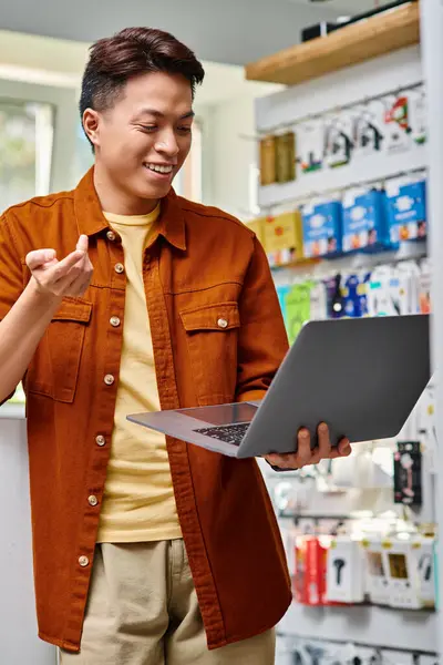 Веселый азиатский бизнесмен с видеозвонком на ноутбуке в частном магазине современной электроники — стоковое фото