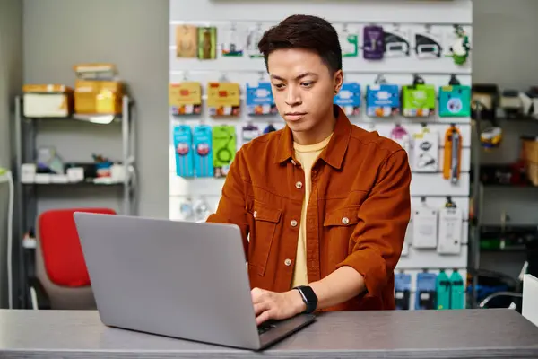 Серьезный азиатский человек с помощью ноутбука на прилавке в частном магазине электроники, концепция малого бизнеса — стоковое фото