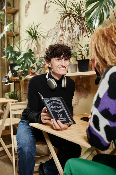 Cheerful young man holding menu near curly african american girl in a plant-filled vegan cafe — Stock Photo