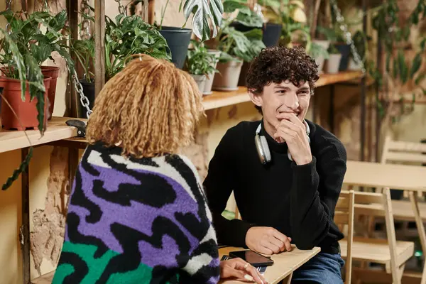Щасливий молодий чоловік в навушниках сміється під час спілкування з афроамериканською дівчиною в веганському кафе — стокове фото
