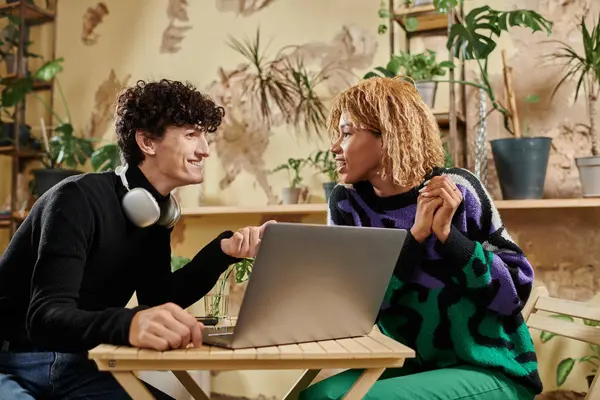 Mujer afroamericana positiva en frenillos mirando novio rizado cerca de la computadora portátil en la cafetería vegana - foto de stock