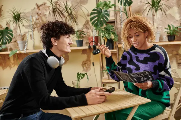 Happy african american woman with braces holding menu and gesturing near boyfriend in vegan cafe — Stock Photo