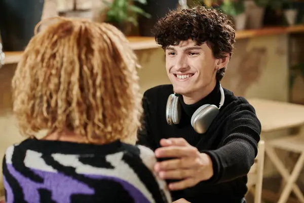 Curly young man with wireless headphones touching shoulder of african american girl in vegan cafe — Stock Photo