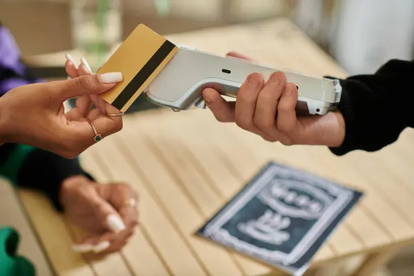 Cliente feminino segurando cartão de crédito perto leitor de cartão, mão cortada na mulher que paga no café vegan — Fotografia de Stock