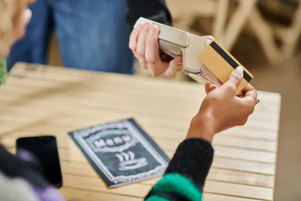 Молодий клієнт тримає кредитну картку біля читача карт, обрізаний рукою на жінку, що платить у веганському кафе — стокове фото