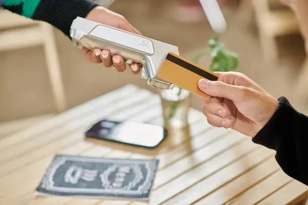 Cliente masculino que sostiene la tarjeta de crédito cerca del lector de tarjetas, la mano recortada en el hombre que paga en la cafetería vegana - foto de stock