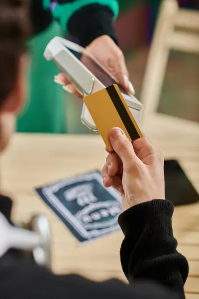 Cliente que sostiene la tarjeta de crédito cerca del lector de tarjetas sin contacto, mano recortada del hombre que paga en la cafetería vegana - foto de stock