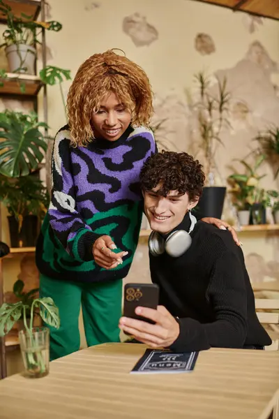 Щаслива мультикультурна пара з кучерявим волоссям, дивлячись на смартфон і вибираючи меню в веганському кафе — стокове фото