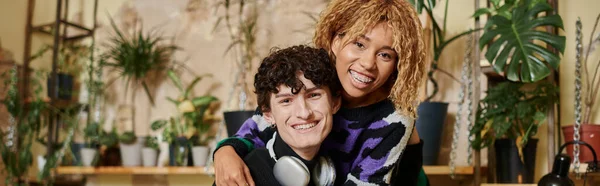 Cheerful african american woman with braces embracing curly young man in vegan cafe, banner — Stock Photo
