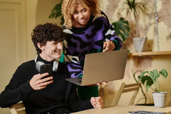 Joyful african american woman holding laptop and embracing boyfriend with smartphone in vegan cafe — Stock Photo