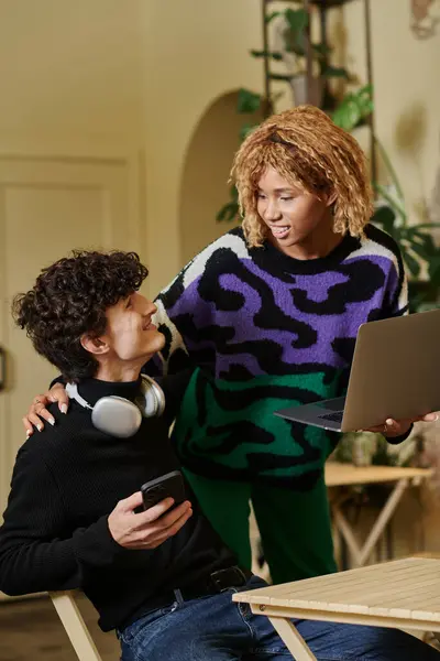 Joyful african american woman with braces holding laptop and embracing boyfriend with smartphone — Stock Photo