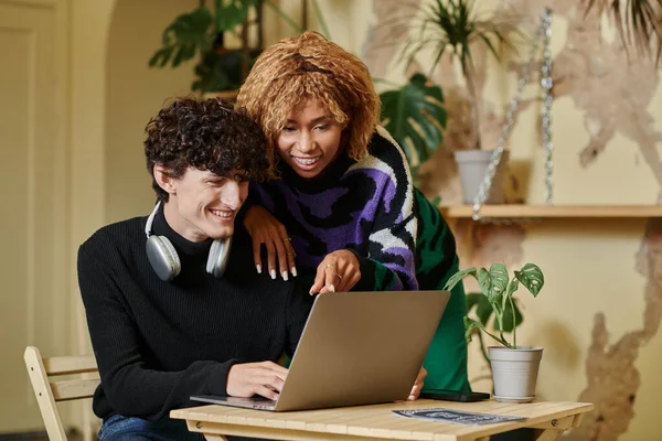 Glücklich afrikanisch-amerikanische Frau mit Zahnspange umarmt lockigen Freund und Blick auf Laptop im Café — Stockfoto