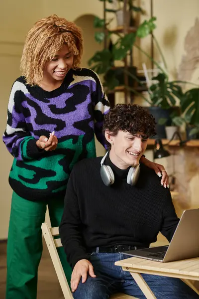 Smiling african american girl with braces hugging curly boyfriend and looking at laptop in cafe — Stock Photo