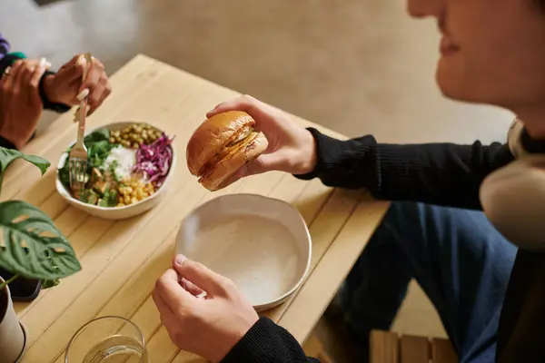 Ritagliato giovane uomo godendo pasto vegan mentre tenendo hamburger con tofu vicino donna offuscata mangiare insalata — Foto stock