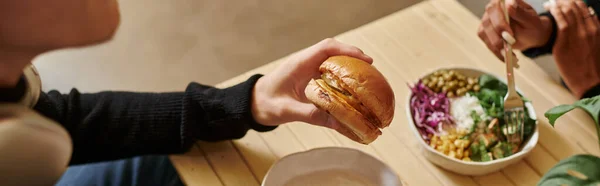 Bannière de l'homme dégustant un repas végétalien tout en tenant un hamburger avec du tofu près de femme floue manger de la salade — Photo de stock