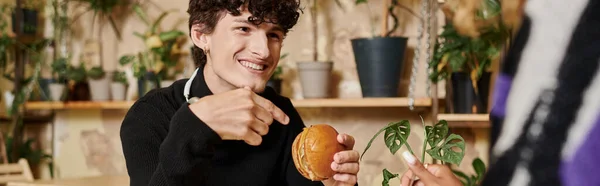 Joyful young man in headphones holding tofu burger and looking at african american woman, banner — Stock Photo