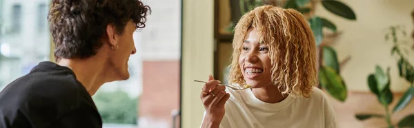 Happy african american woman with braces eating salad near blurred boyfriend in vegan cafe, banner — Stock Photo
