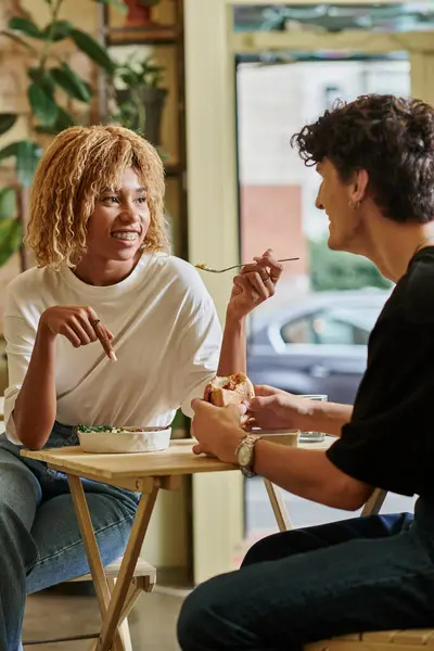 Glücklich afrikanisch-amerikanische Frau mit Zahnspange isst Salat in der Nähe unscharfen Lockenkopf Freund in veganem Café — Stockfoto