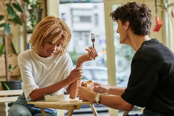 Cheerful african american woman with braces eating salad near blurred curly boyfriend in vegan cafe — Stock Photo