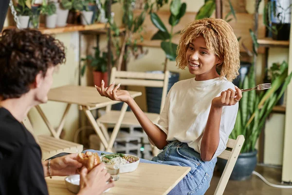 Felice donna africana americana con chiacchierare con il fidanzato riccio vicino pasto vegetariano in caffè vegan — Foto stock