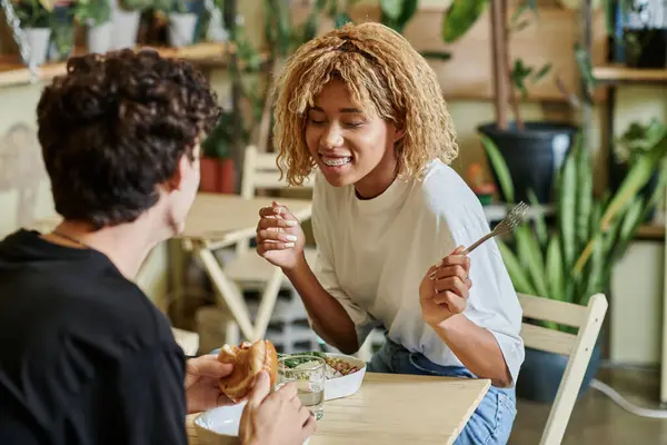 Aufgeregtes afrikanisch-amerikanisches Mädchen plaudert mit lockigem Freund in der Nähe pflanzlichen Essens im veganen Café — Stockfoto