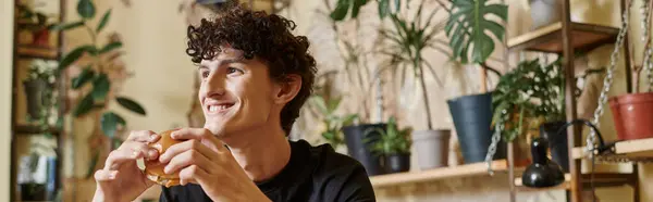 Happy young man holding tofu burger and looking away while smiling in vegan cafe, enjoyment banner — Stock Photo