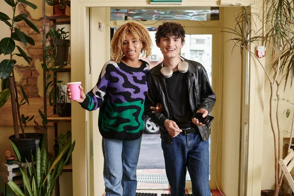 Позитивная разноплановая пара в повседневной одежде, смотрящая в камеру, стоя вместе в веганском кафе — стоковое фото