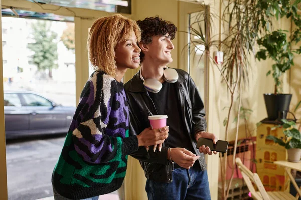 Sourire couple diversifié en tenue décontractée regardant loin tout en se tenant ensemble dans un café végétalien — Photo de stock