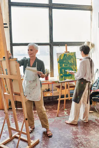 Talented middle aged women in aprons painting on easels in modern art workshop, creative hobby — Stock Photo