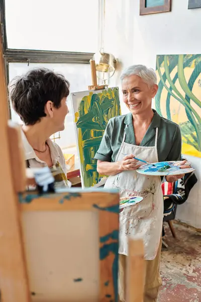 Talented female friends with color palettes in modern painting studio, creative art and friendship — Stock Photo