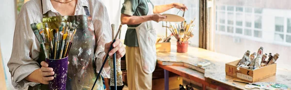 Cropped view of mature female artists choosing paintbrushes in crafts workshop, horizontal banner — Stock Photo