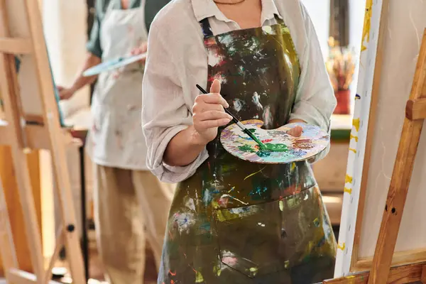 Cropped view of mature woman in apron mixing paints on color palette, master class in art workshop — Stock Photo