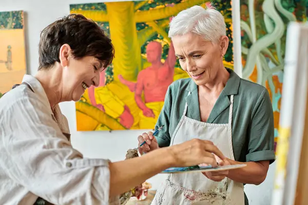 Cheerful mature women mixing paints on color palette during painting master class in art studio — Stock Photo