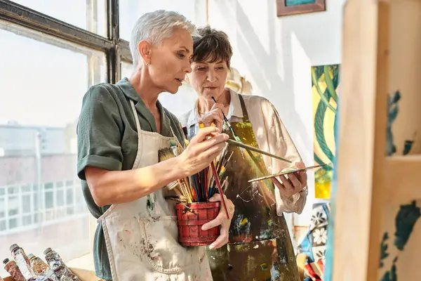 Talented mature female artists choosing  paintbrushes during master class in craft workshop — Stock Photo