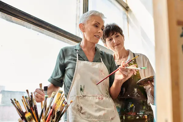 Жінка середнього віку художник вибирає пензлі біля жіночих друзів під час майстер-класу в художній студії — стокове фото